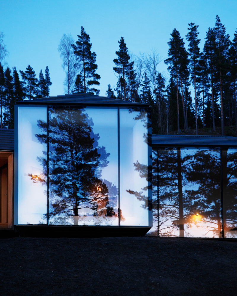 Eksteriør foto av fasade på hytte, stort reflekterende vindu, skog i bakgrunnen. Kvelds setting.