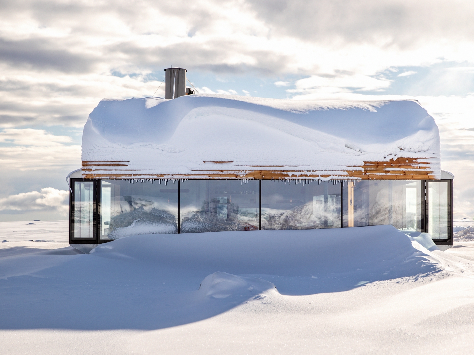 Et bygg i treverk med store vinduer nedsnøet i et vinterlandskap. Foto.