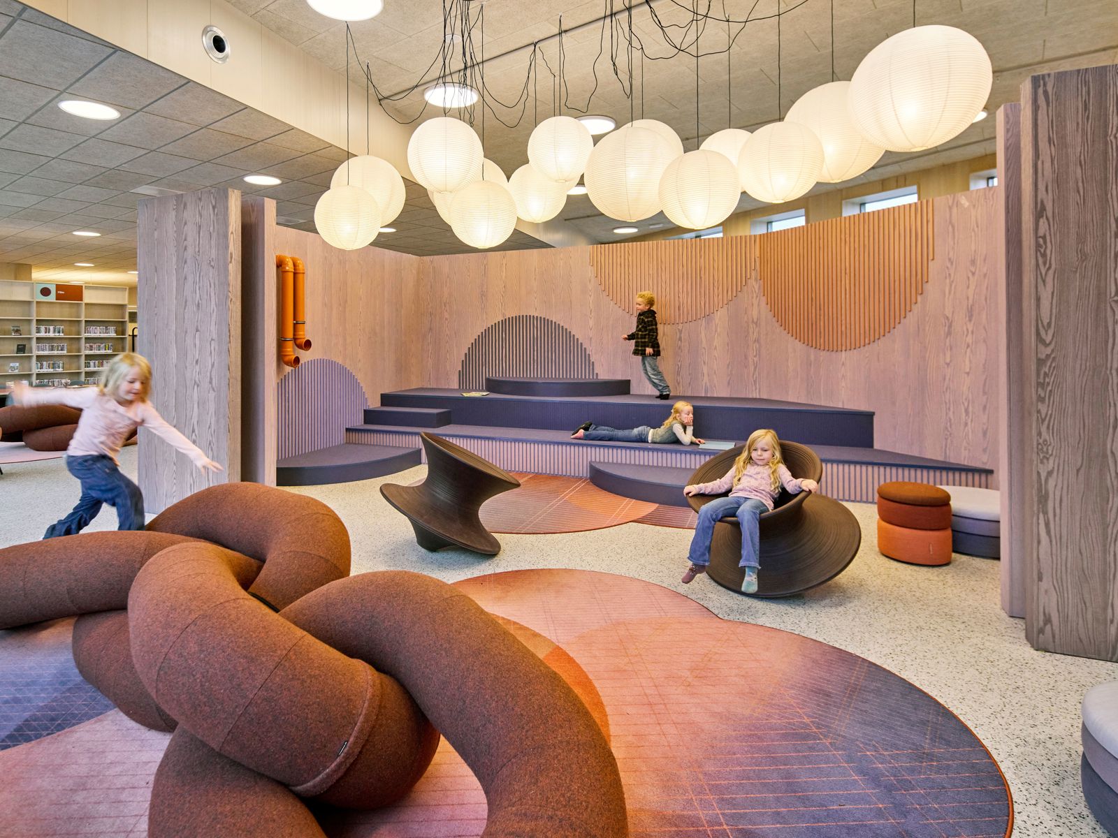 Interiør foto fra barneavdelingen i biblioteket på Steinkjær kulturhus, barn som leker og leser på ulike fargerike møbler i diverse former.