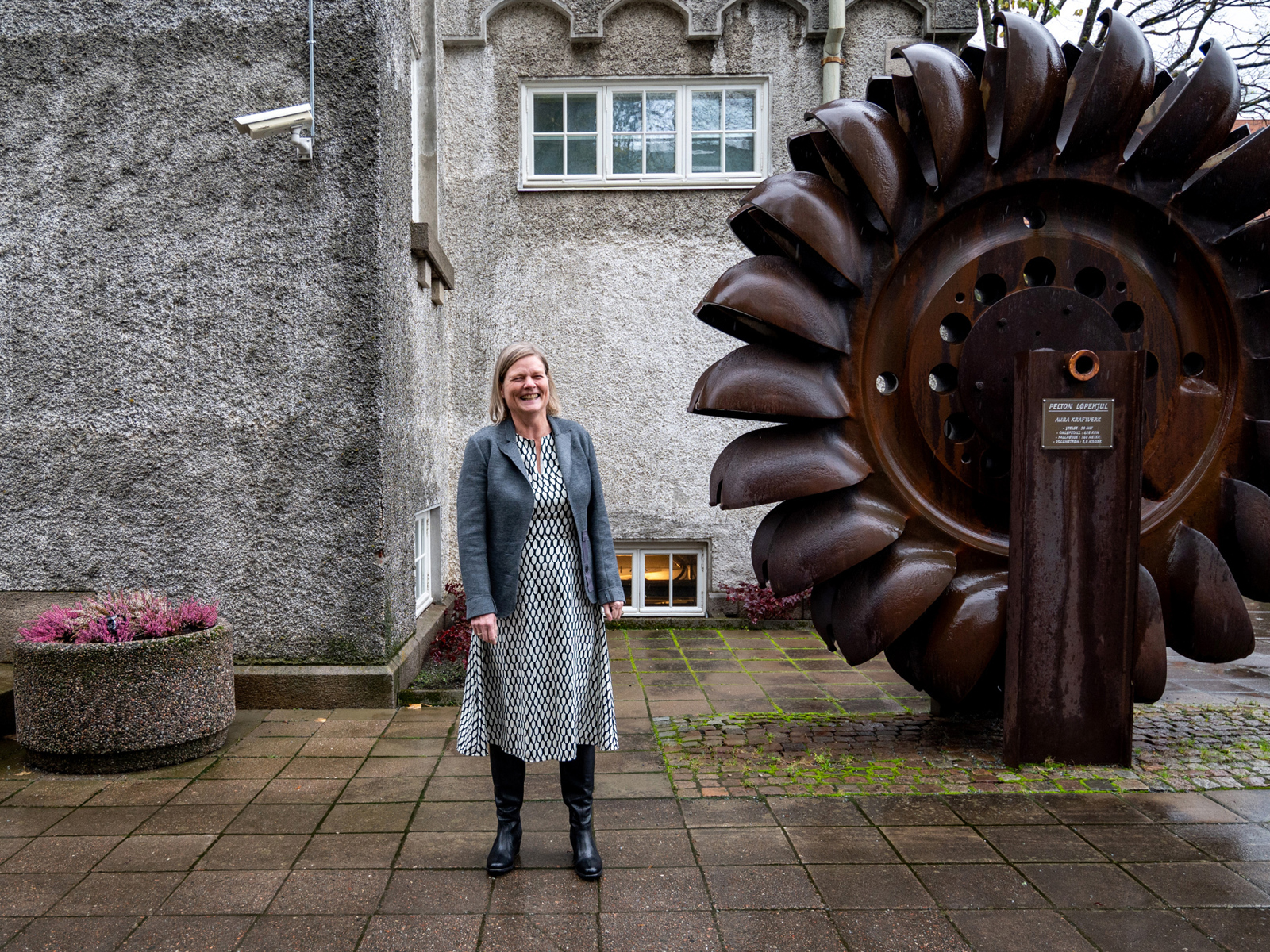 Marianne Skjulhaug utenfor et bygg og vannhjul. Foto.