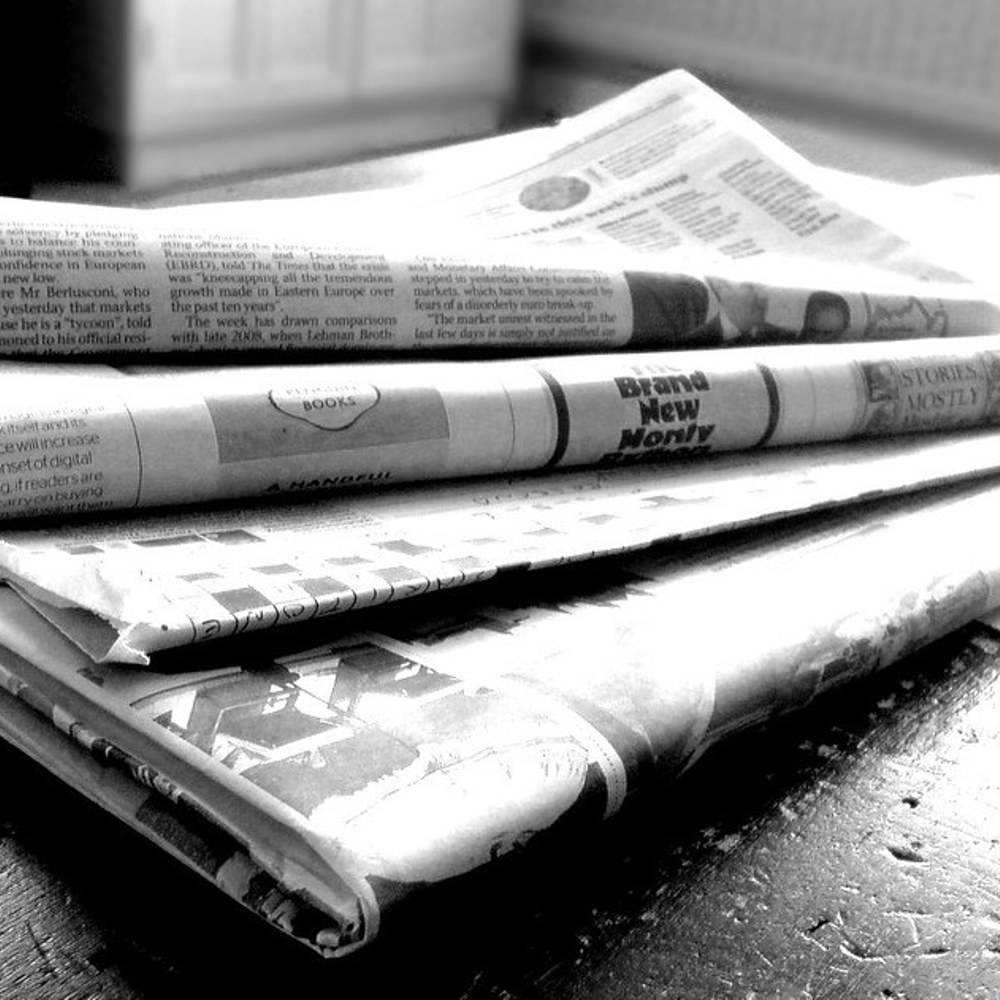 4 aviser brettet sammen og i en haug på et bord, svart hvitt. Foto.