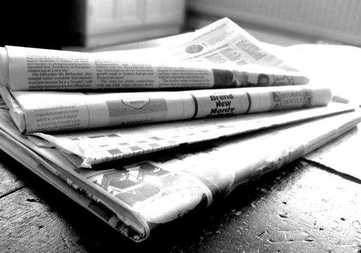 4 aviser brettet sammen og i en haug på et bord, svart hvitt. Foto.