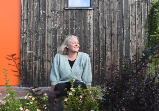 Pernille Kolstad Heen sittende utenfor en trevegg. Foto.