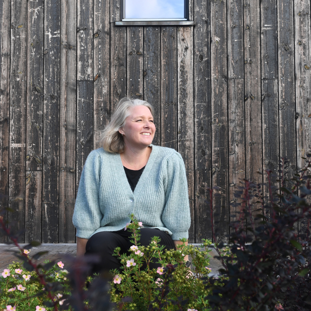 Pernille Kolstad Heen sittende utenfor en trevegg. Foto.