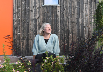 Pernille Kolstad Heen sittende utenfor en trevegg. Foto.