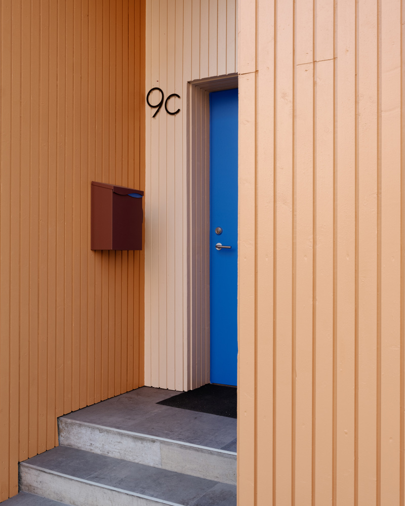 Blå dør i en inntrukket nisje i ulike rose og oransje toner og en rød postkasse. Foto.