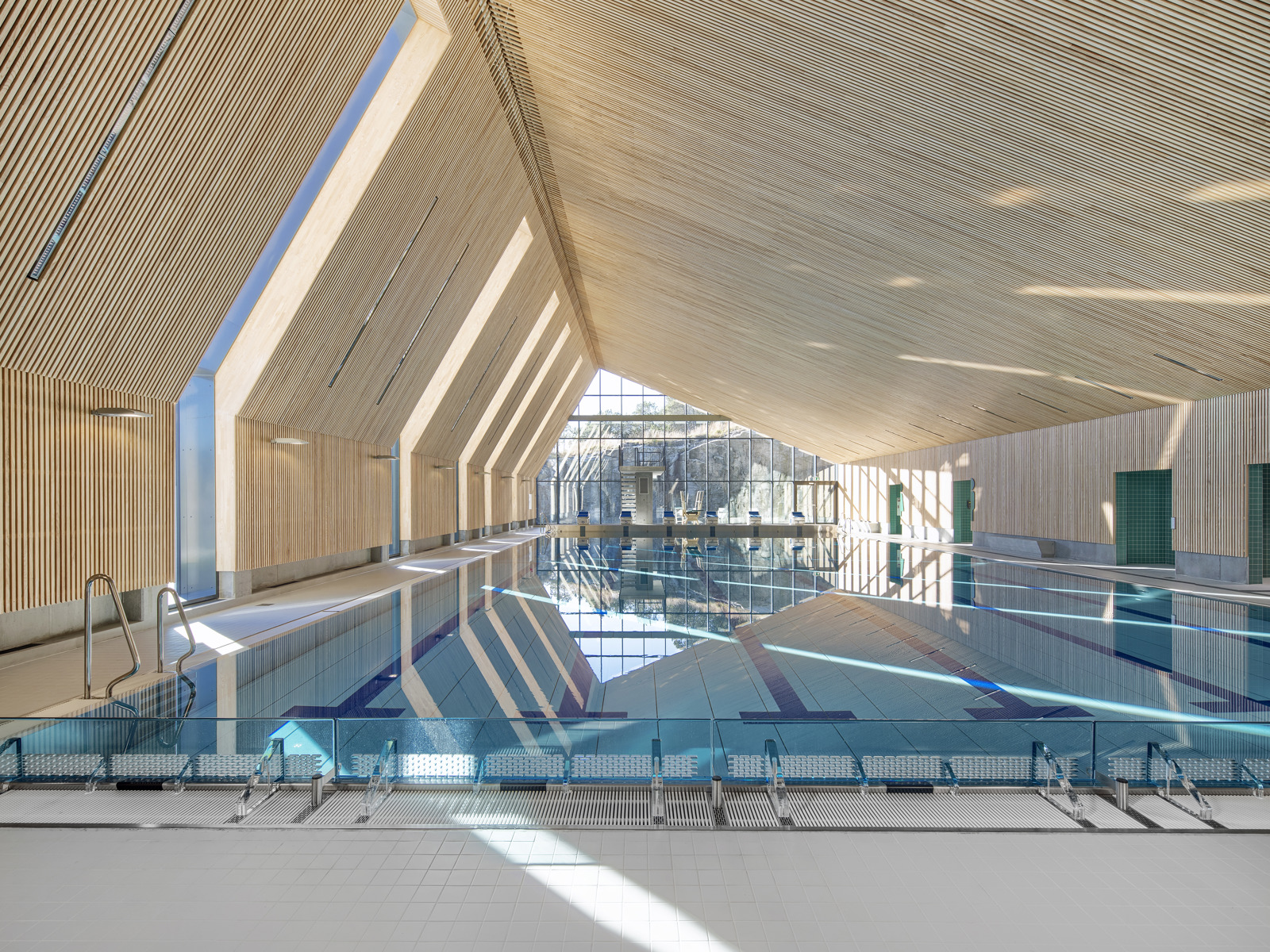 Interiør foto av svømmehall, vinklet tak, stort vindu i enden av basseng.