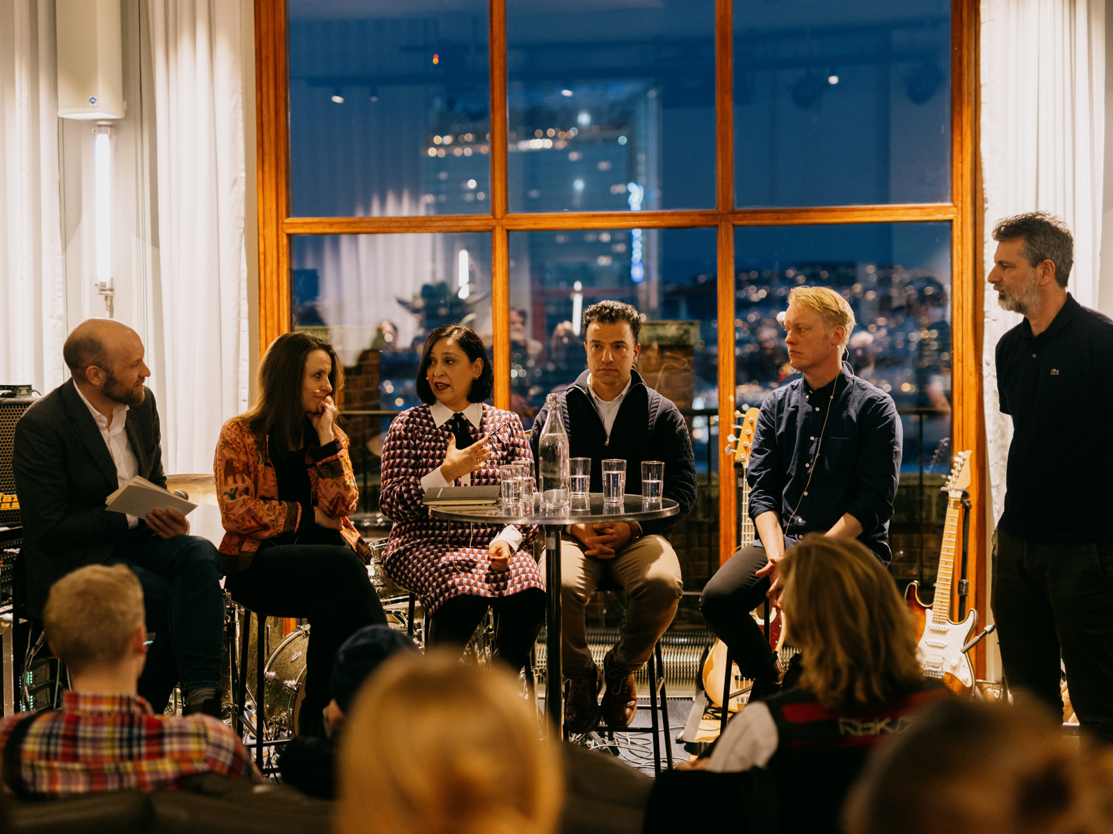Foto av paneldebatt på en scene med vindu i bakgrunnen.