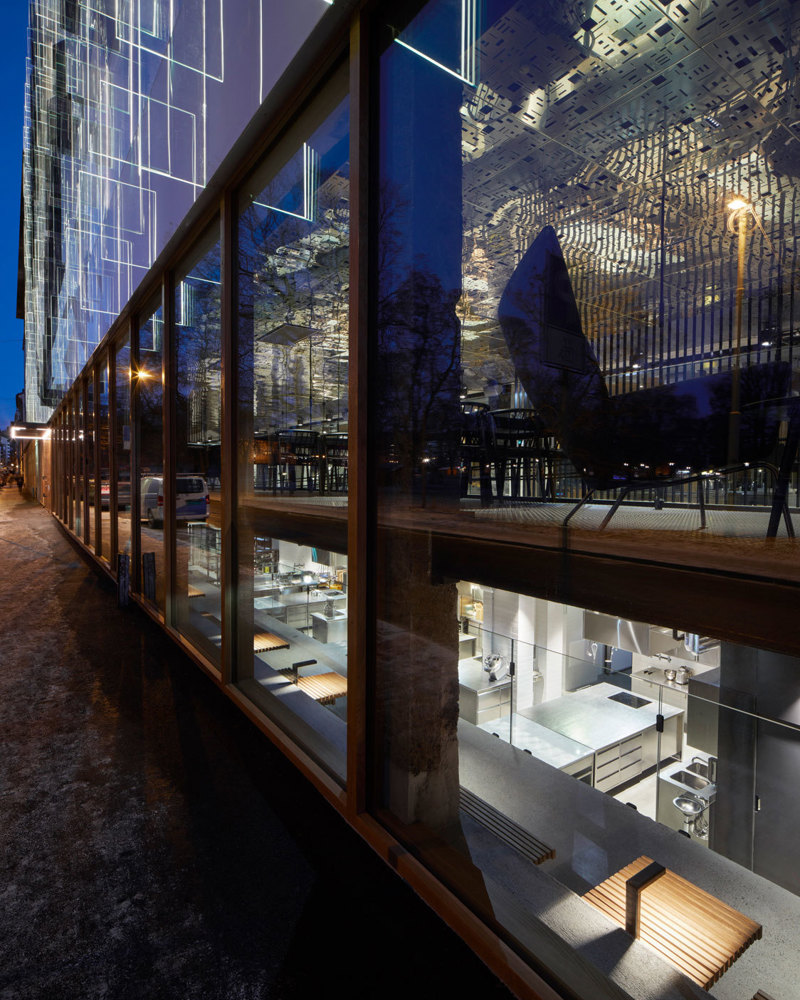 Fotografi inn glassfasade inn til bygg med flere sittegrupper over flere etasjer. Mørkt ute.