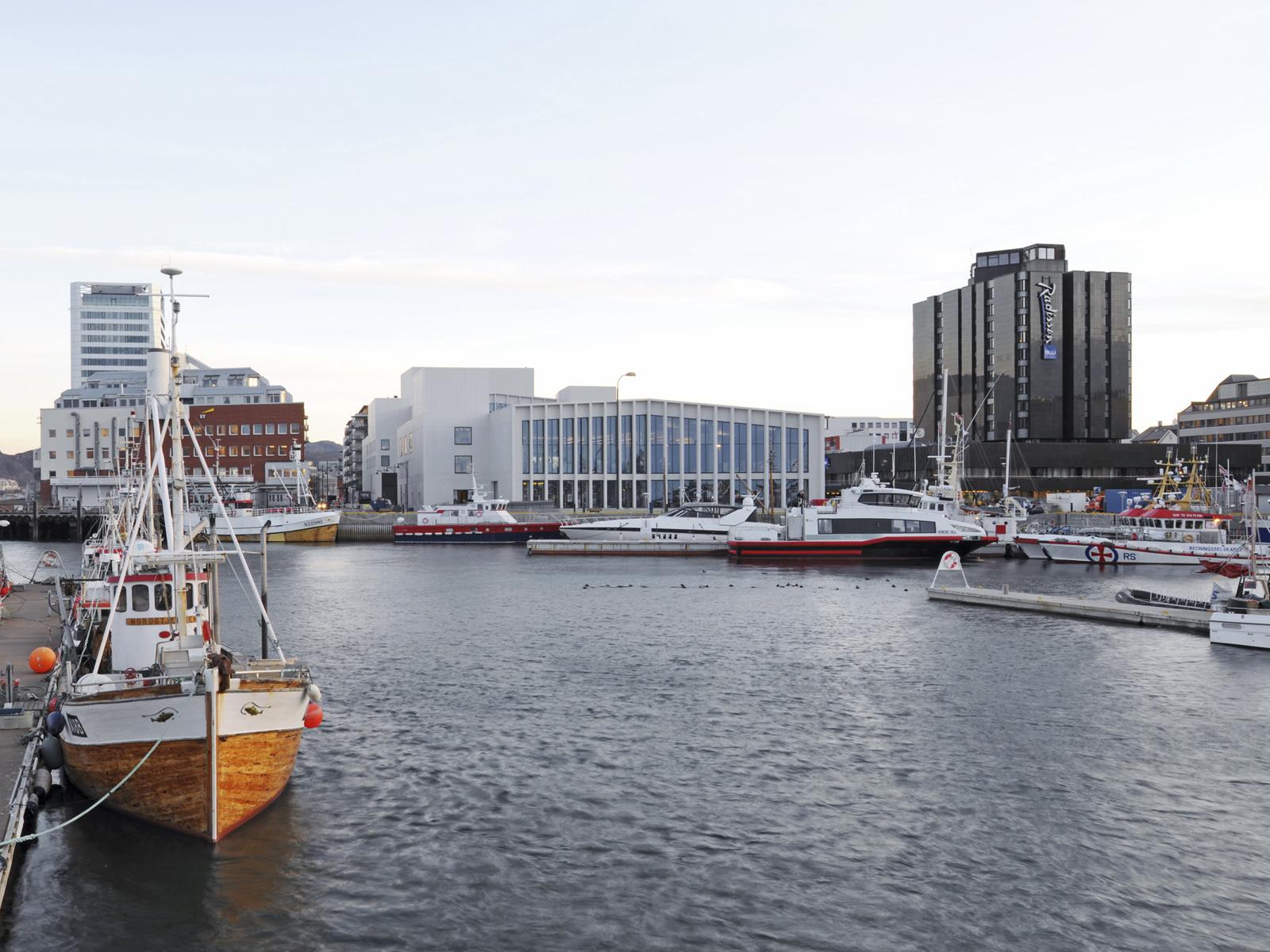 Vann i forgrunnen, kulturhus i bykontekst i bakgrunnen på havnen. Foto.
