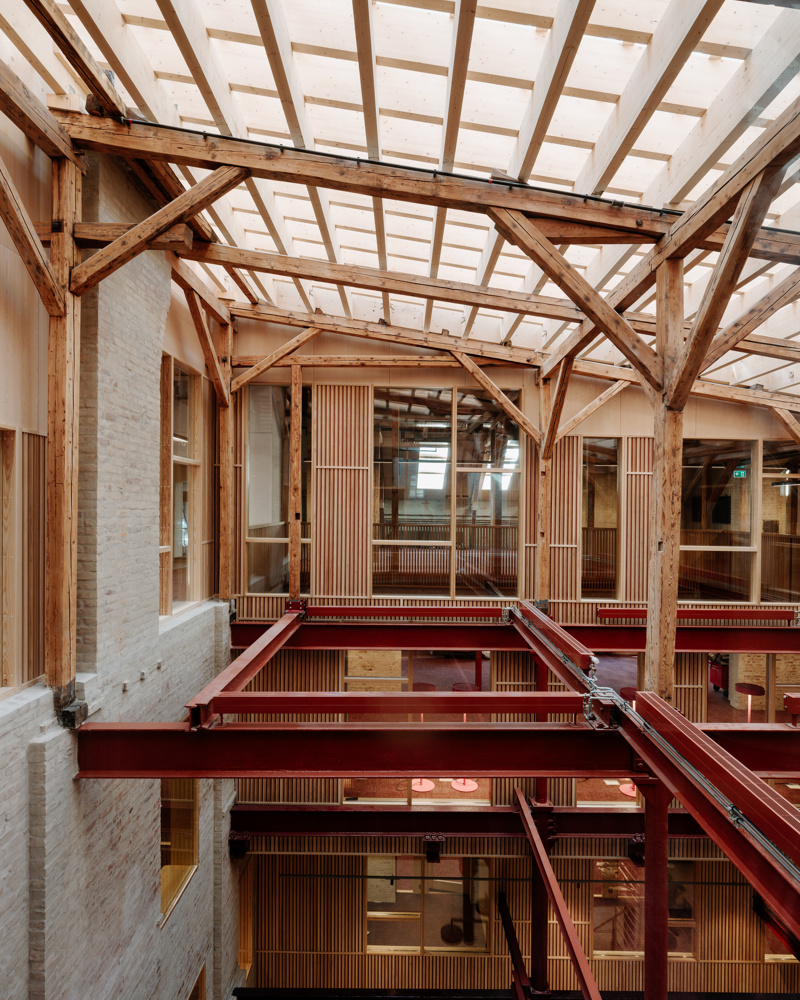 Utsikt inn i atrium med overlys og tidligere etasjeskille bjelker eksponert. Foto.