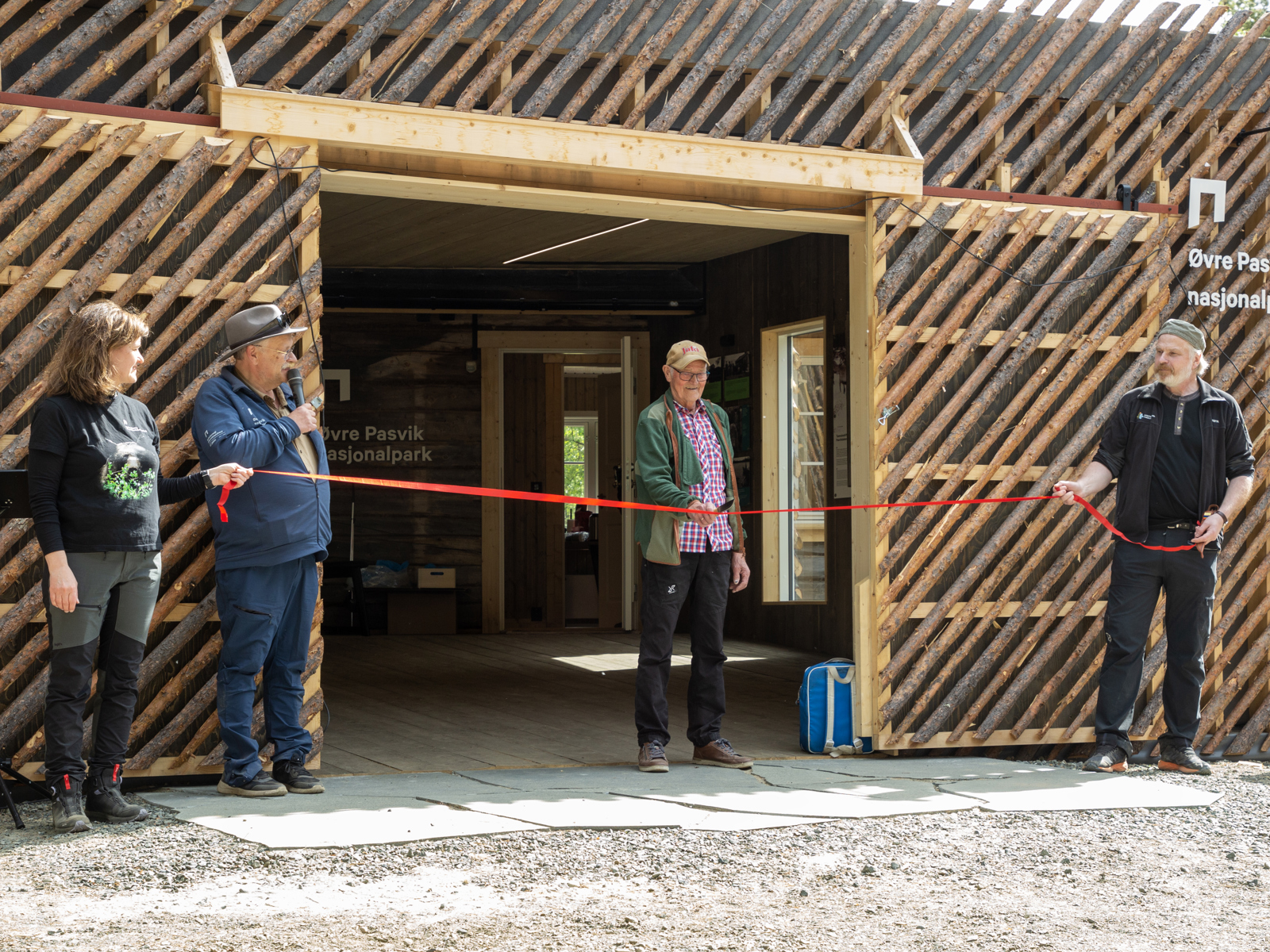 Mann klipper rødt bånd i åpningen på bygg. Foto.