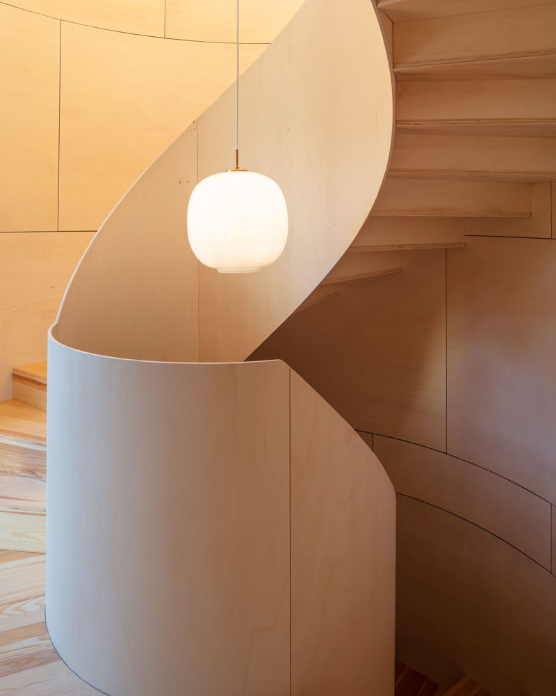 Spiraltrapp i tre med en lampe hengende i midten. Foto.