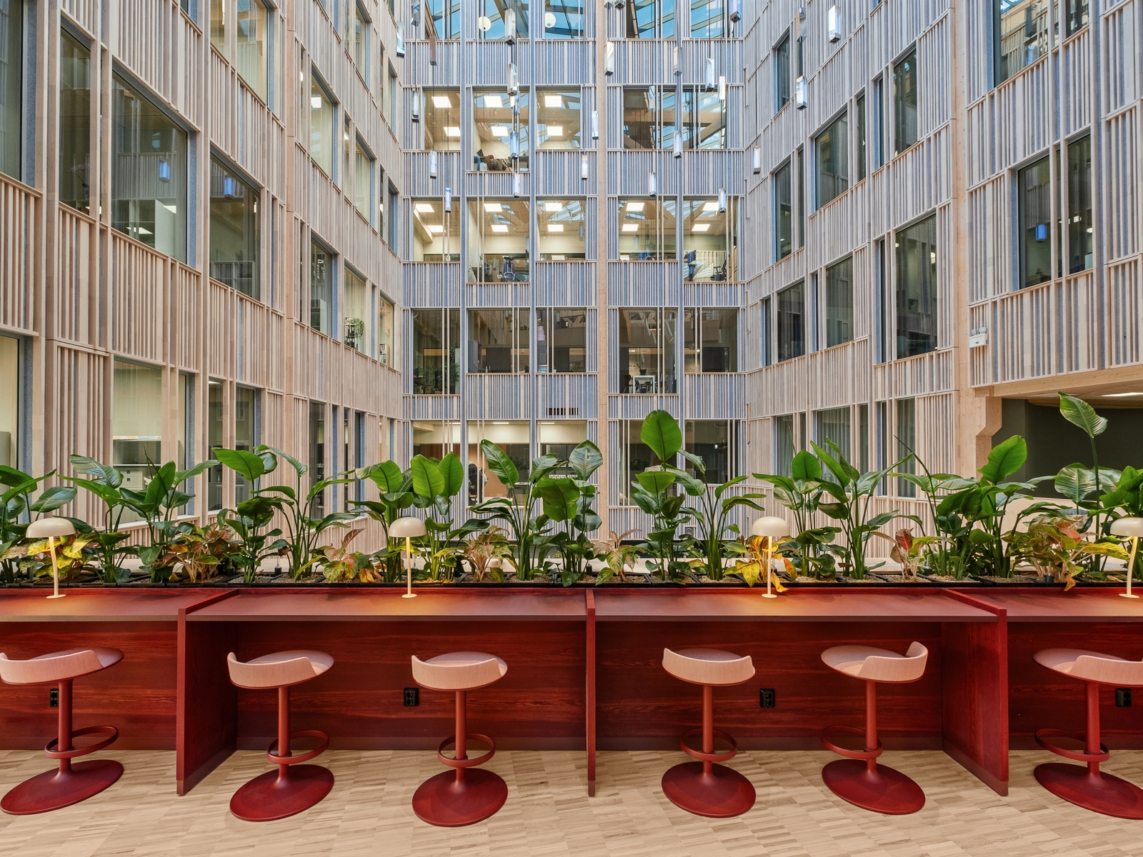 Interiør foto av atrium i campus bygg, rød barbenk med røde barstoler og grønne planter ut mot det åpne rommet.