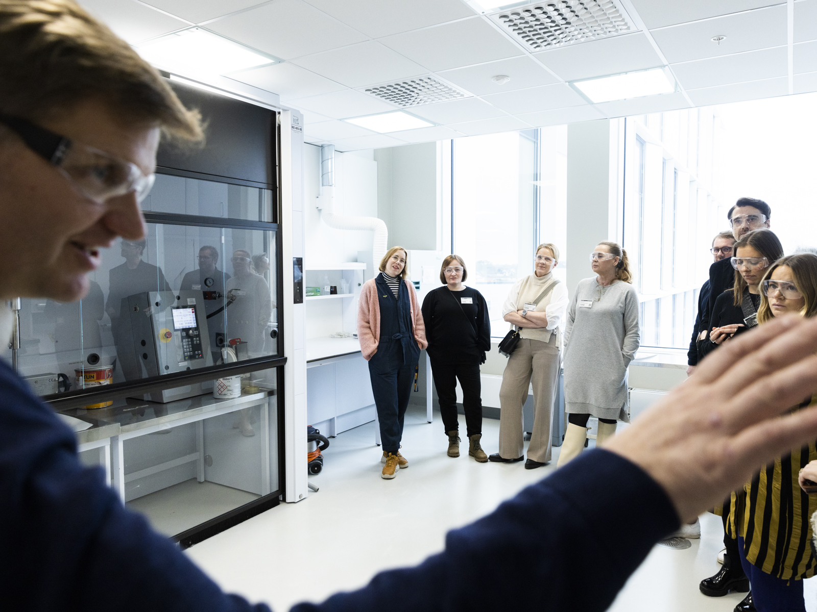 Mann peker i forgrunnen, mennesker lytter i bakgrunnen. Foto.