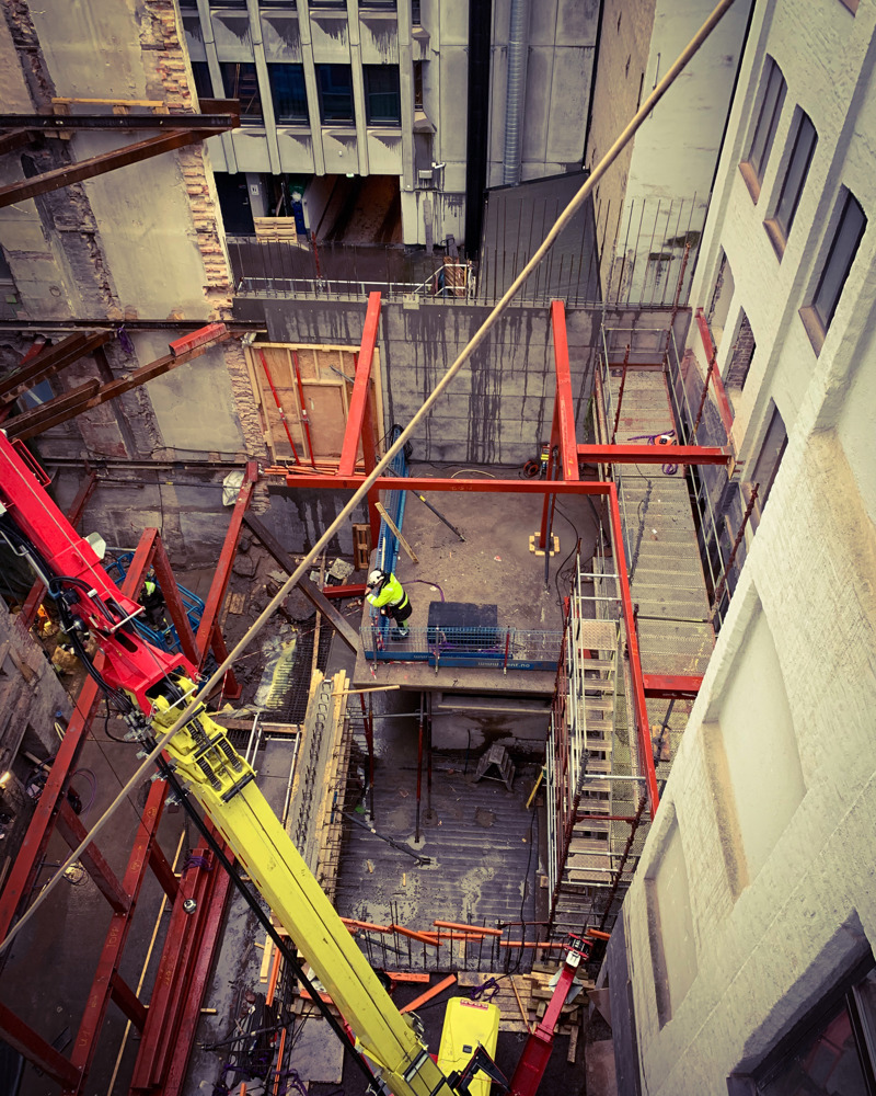 Byggeplass, kran og stilas mellom bygg. Foto.