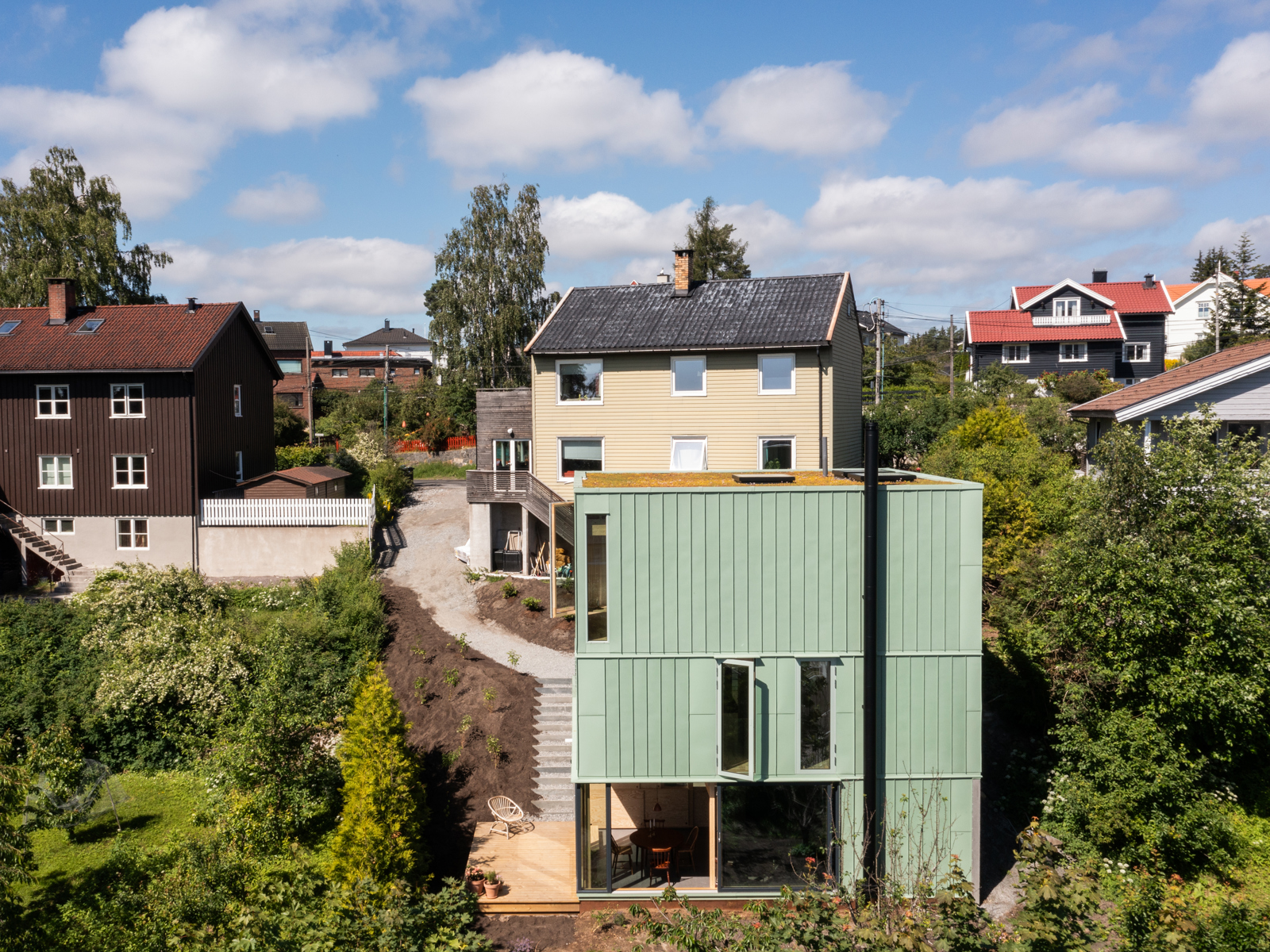 Eksteriørfoto av enebolig med grønn kobberfasade i skråning.