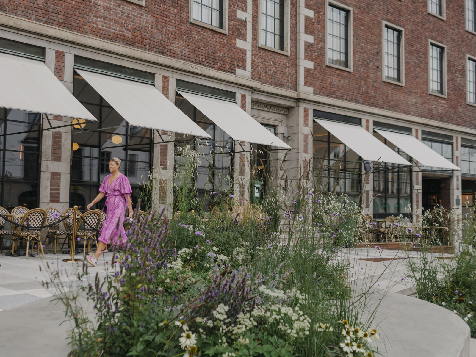 Foto av beplantning fremfor Sommerro, en kvinne i rosa kjole går i bakgrunnen.