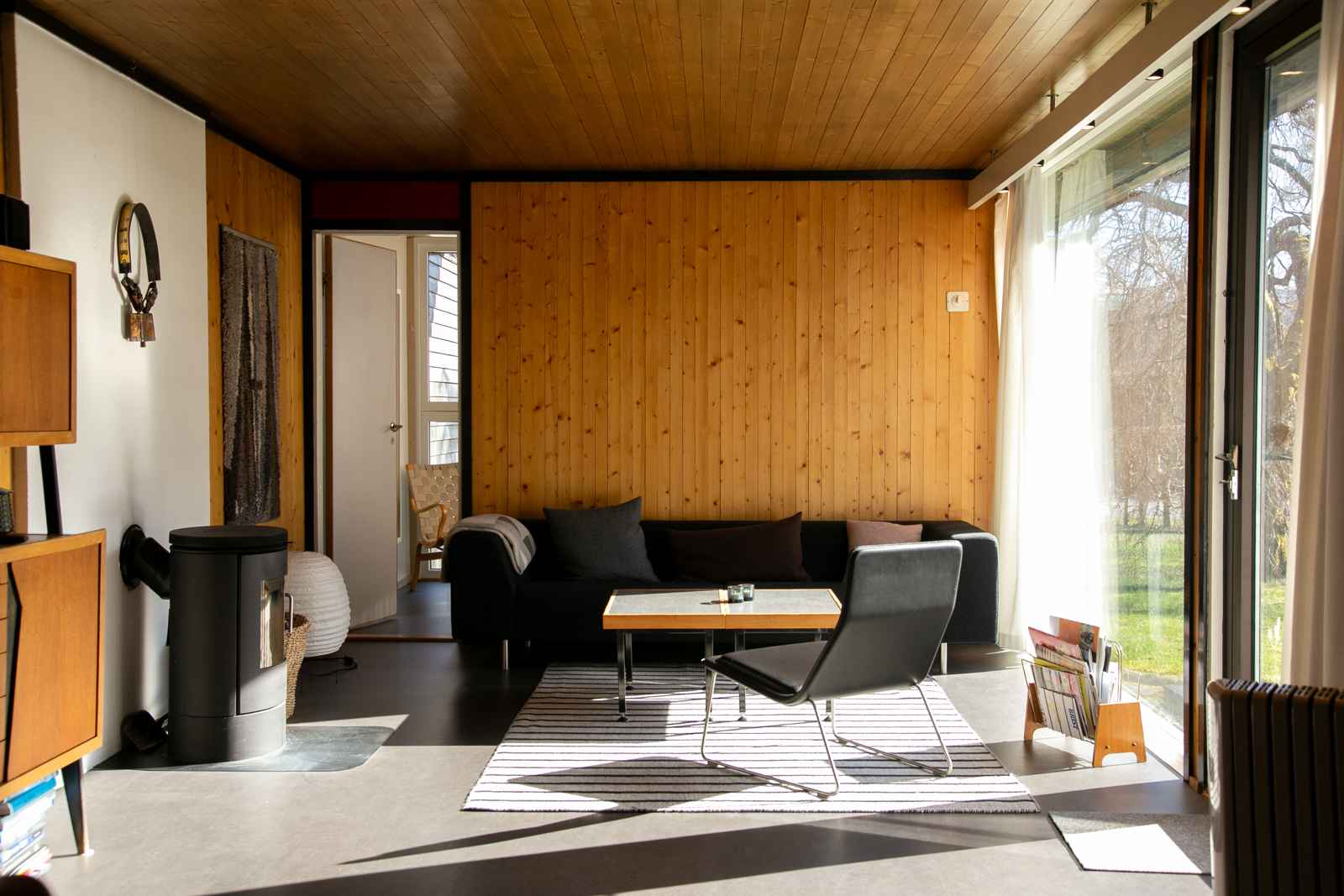 Interiørfoto av stuen fra de enkle bolighusene på Nesflaten. Linoleum på gulvet, mens vegger og tak er i trepanel.
