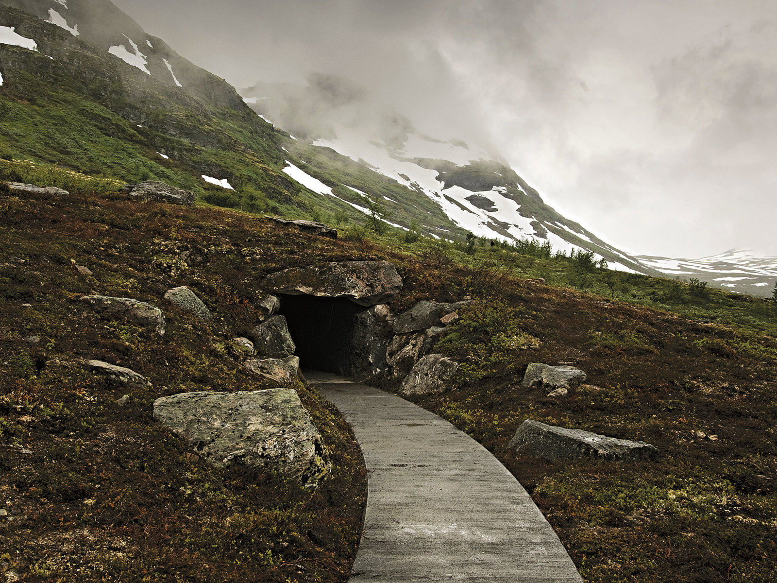 Foto av sti som leder til inngangen på et hule i fjellet.
