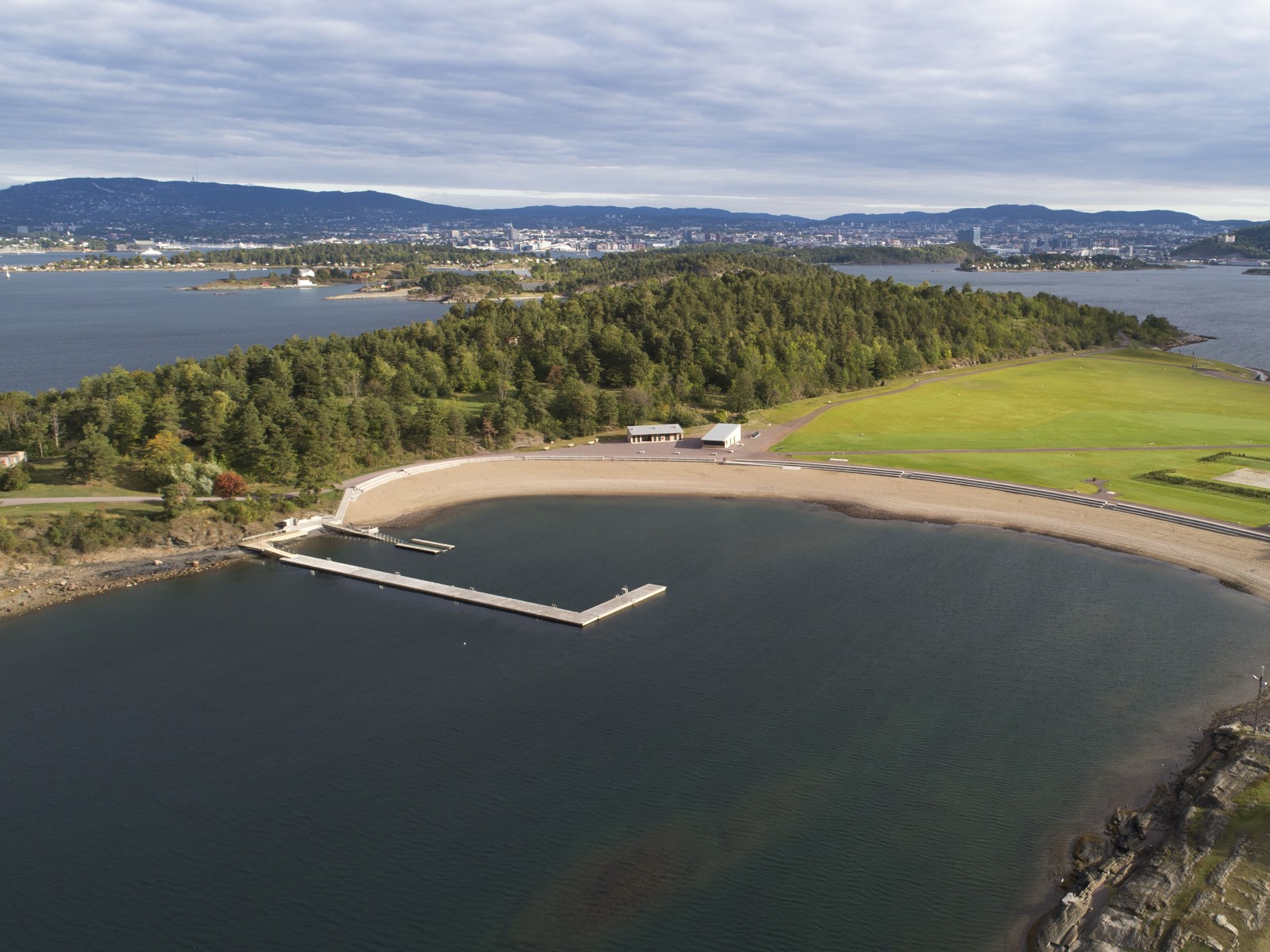 Fly foto av badeanlegg og sandstrand på Langøyene, Oslo i bakgrunnen.