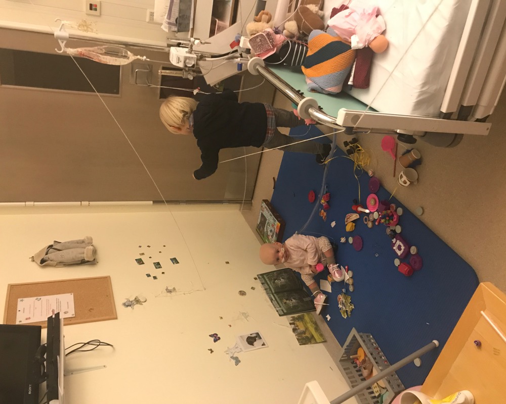 Foto av to barn som leker på gulvet på et sykehusrom.