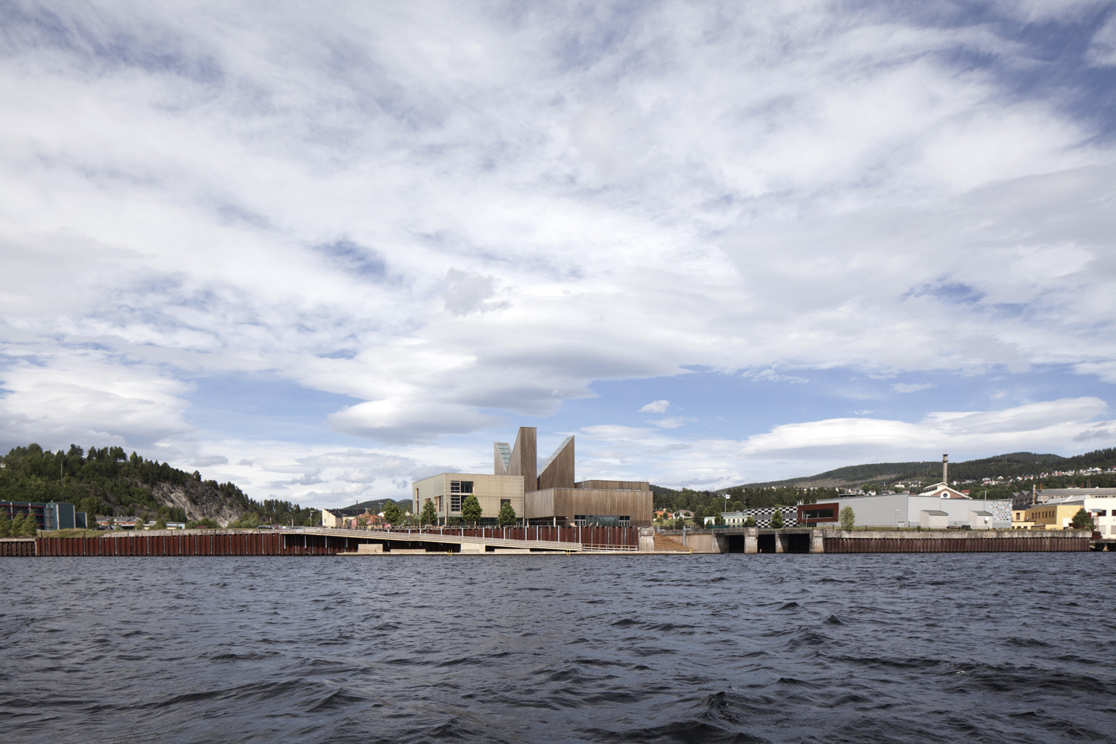 Hav i forgrunnen, brygge og større bygg på land, by bakenfor. Arkitekt tegning.