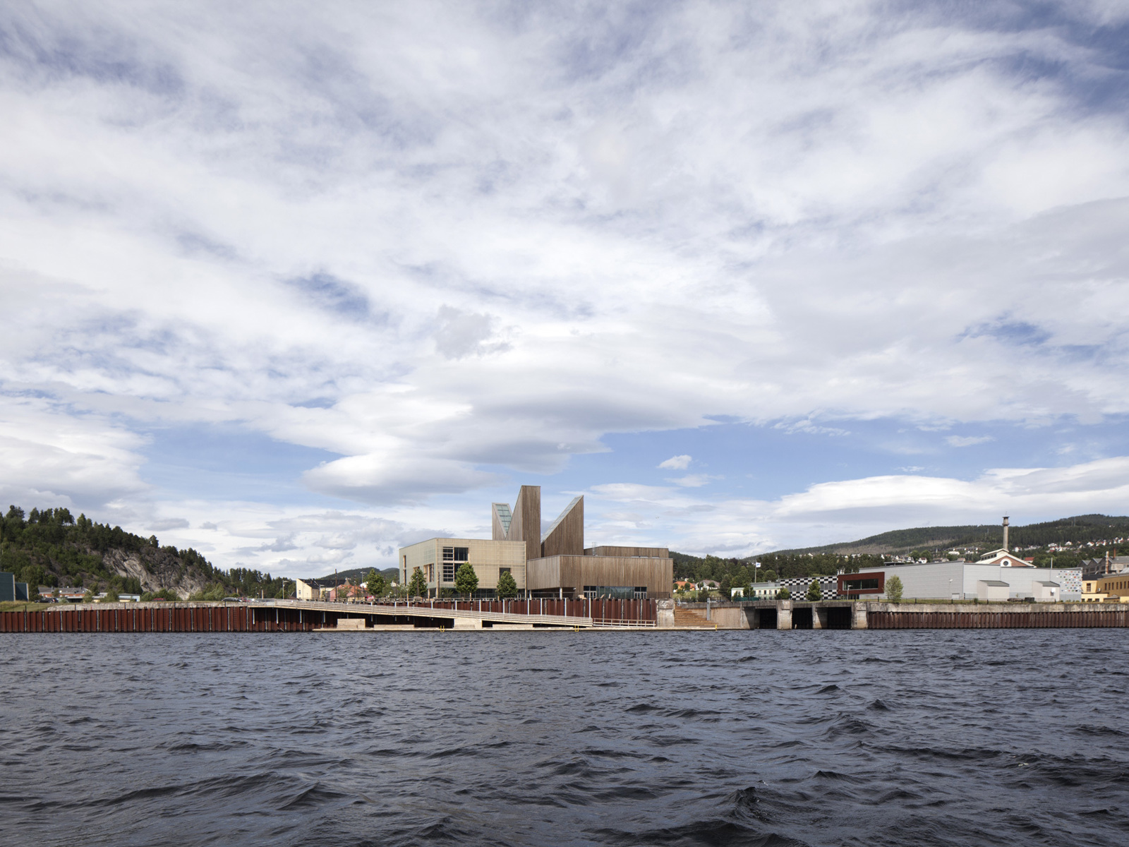 Hav i forgrunnen, brygge og større bygg på land, by bakenfor. Arkitekt tegning.