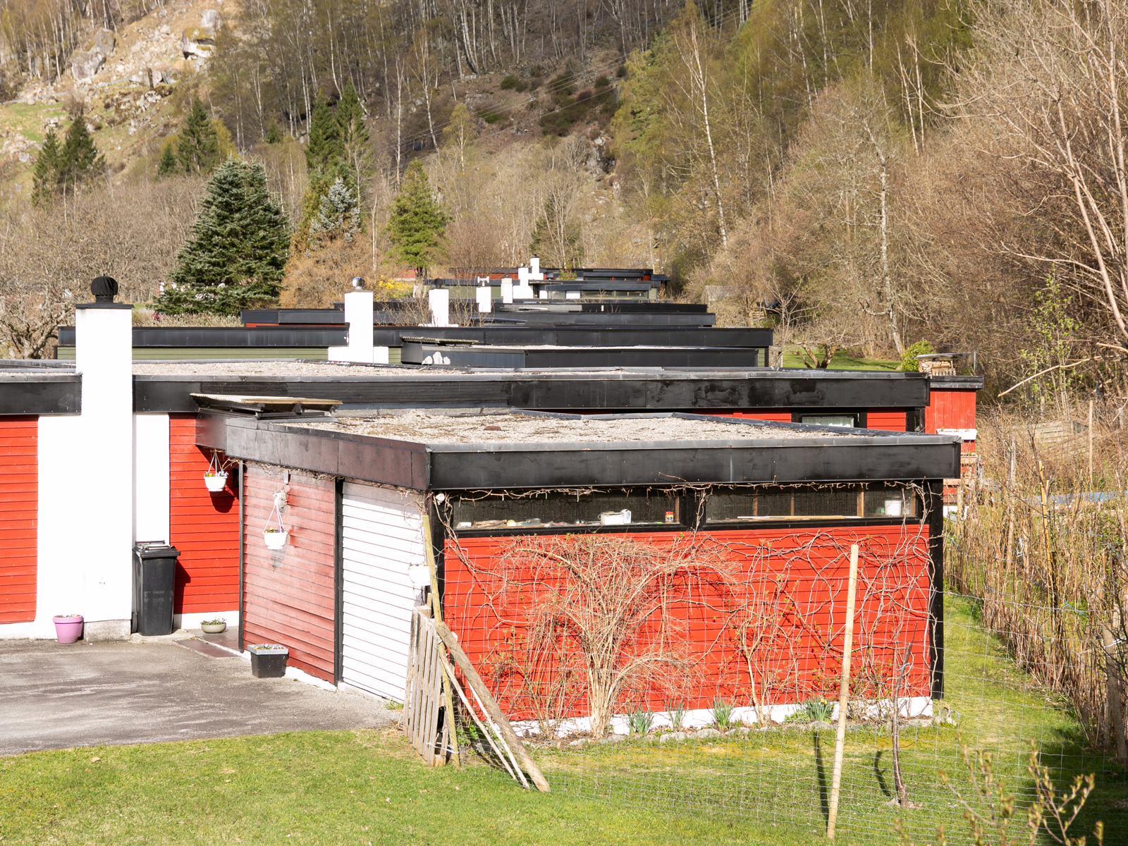Eksteriørbilde av de enkle bolighusene på Nesflaten. Liggende trekledning malt i rødt, med hvit garasjedør og sorte vinduskarmer. 