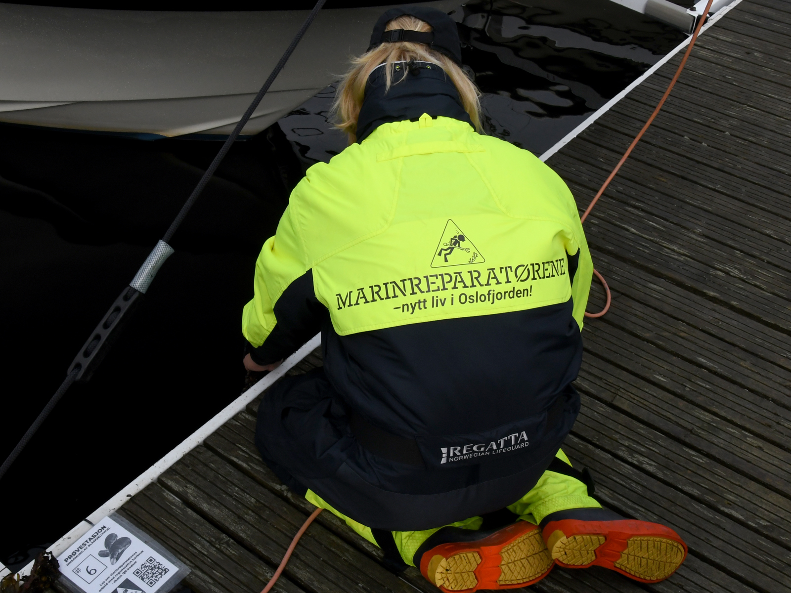 Foto av en kvinne som sitter på bryggekanten og ser ned i vannet.