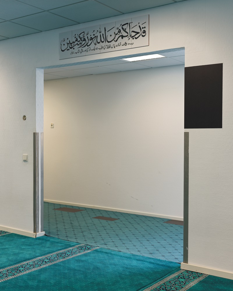 Døråpning, blått teppe på gulvet, arabisk tekst over åpningen. Foto.