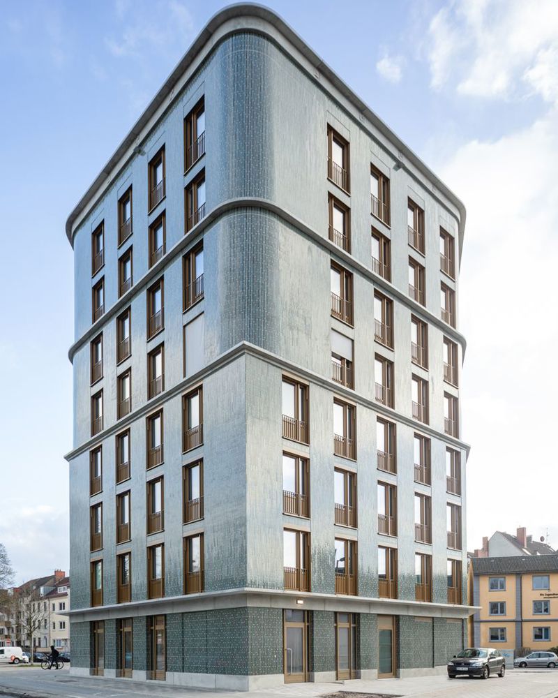 Foto av fasade på en spiss boligblokk, vei i forgrunnen.
