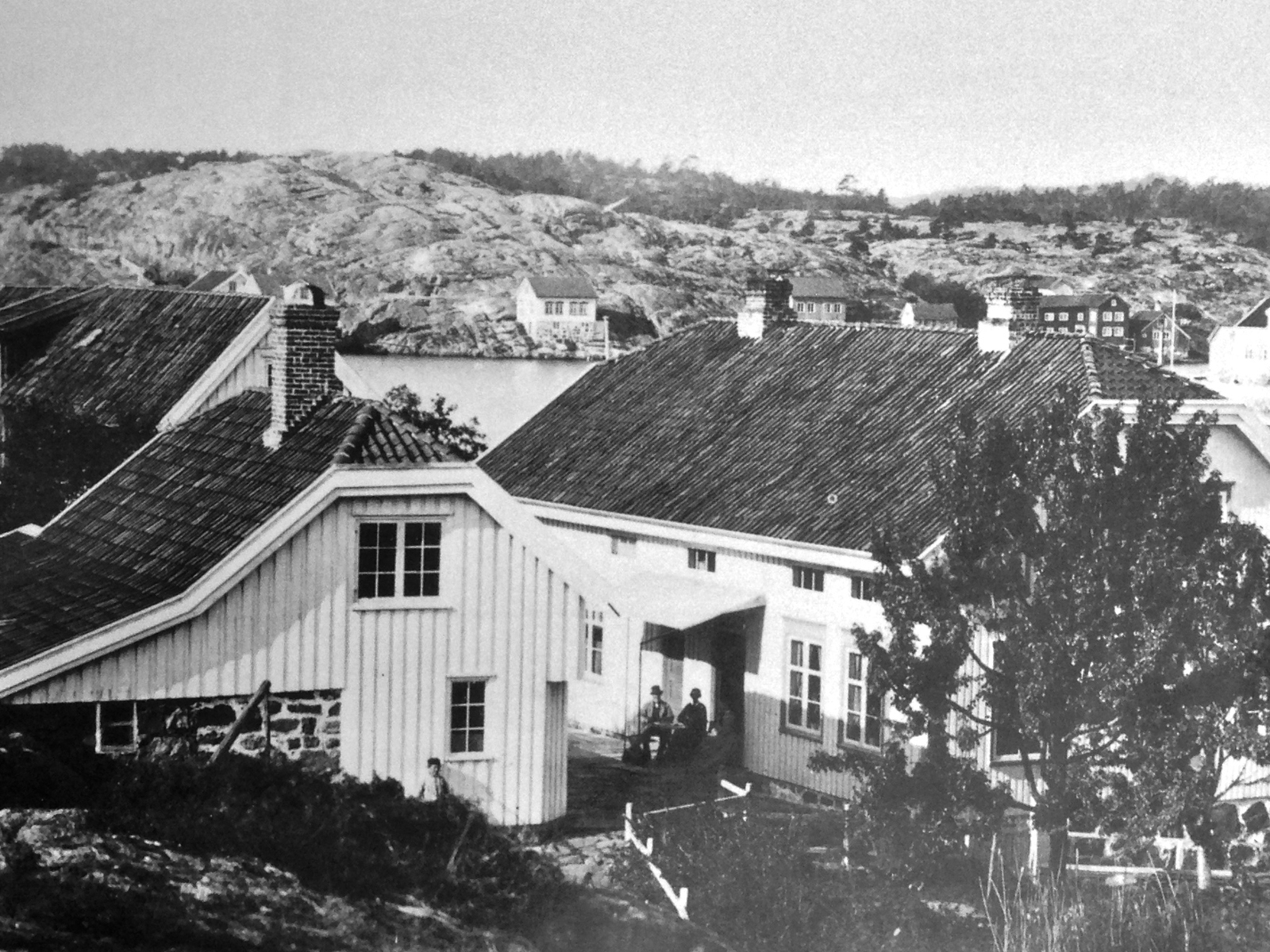 Historisk svart hvitt bilde av flere trebygninger. Foto.