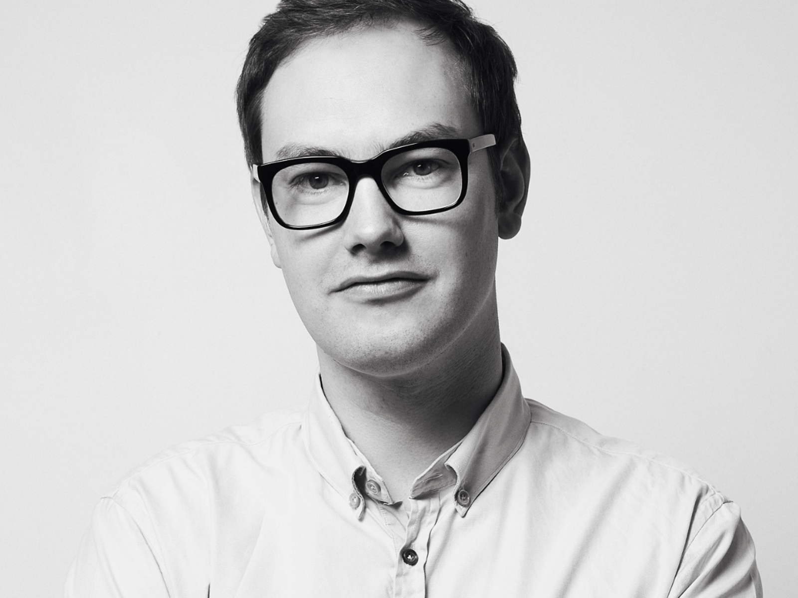 Portrettbilde av Øystein Rø med briller, kort hår og hvit skjorte, svart hvitt. Foto.