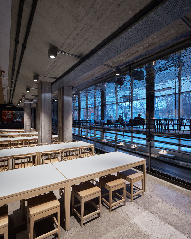 Interiør fotografi av bygg med flere sittegrupper, åpent til etasjen under, messanin og glassfasade.