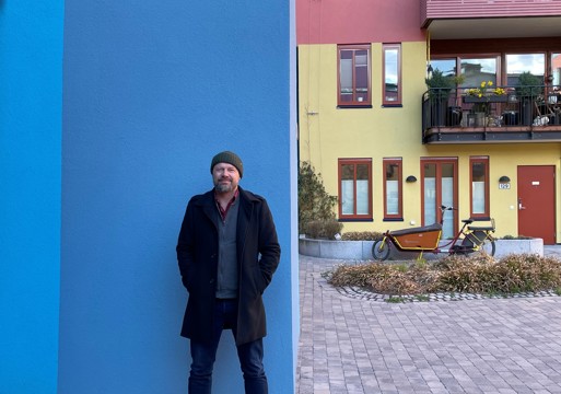 Rasmus Reinvang inntil en blå vegg utendørs, fargerikt bygg i bakgrunnen. Foto