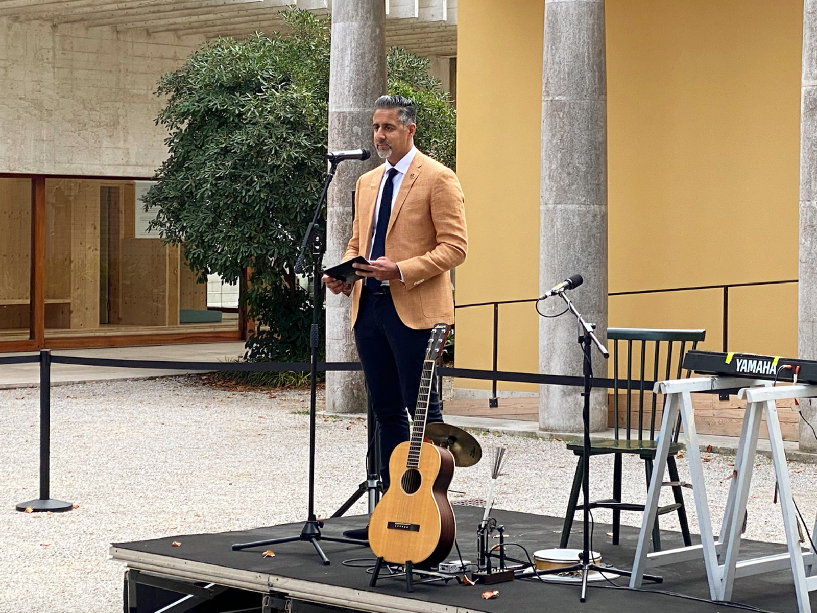 Abid Raja holder tale på en scene utendørs, utenfor den nordiske paviljongen i Venezia. Foto.