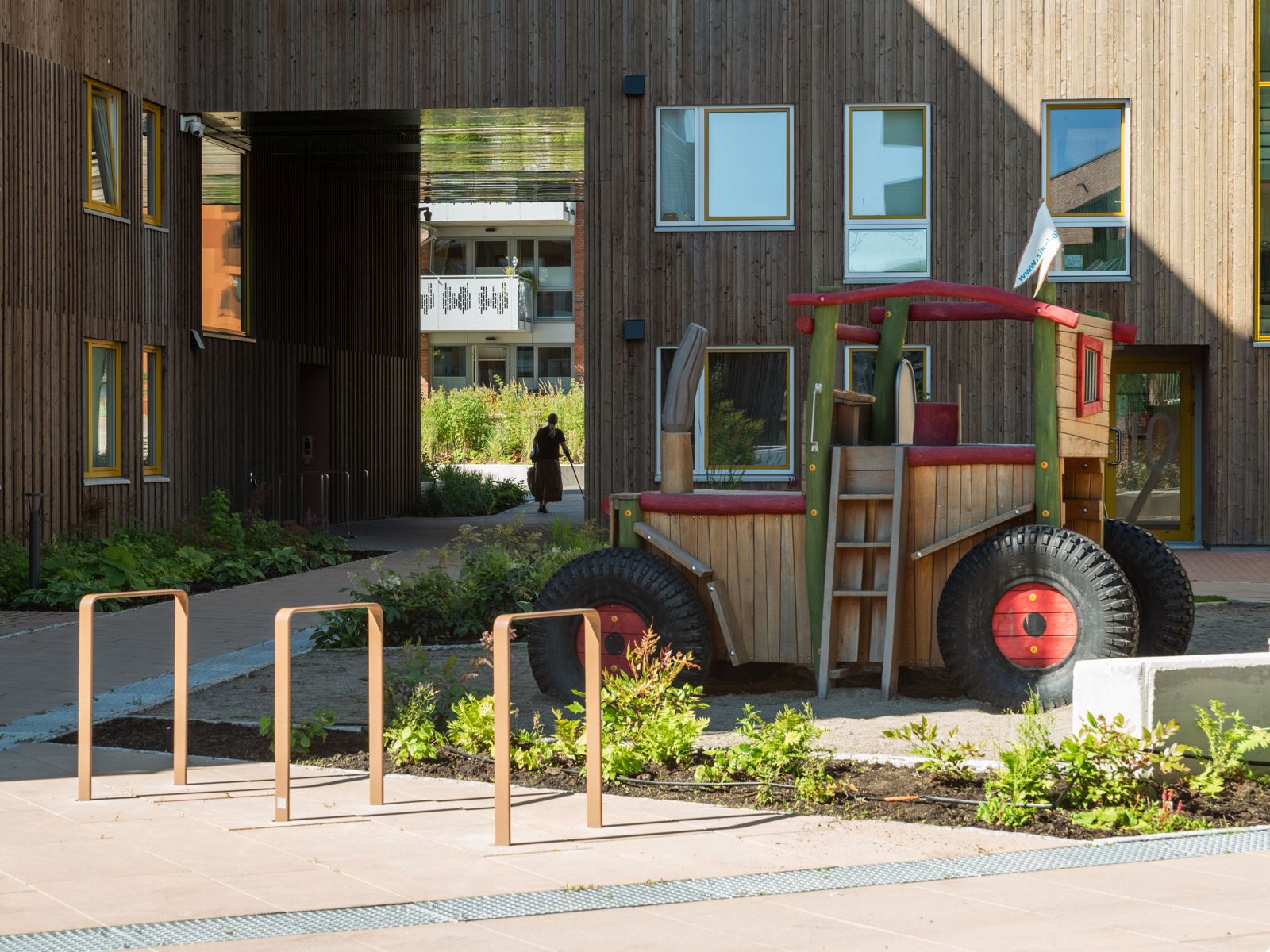 Foto av bakgård i boligkvartal med en leketraktor, portal gjennom bygg og en dame som er ute å går.