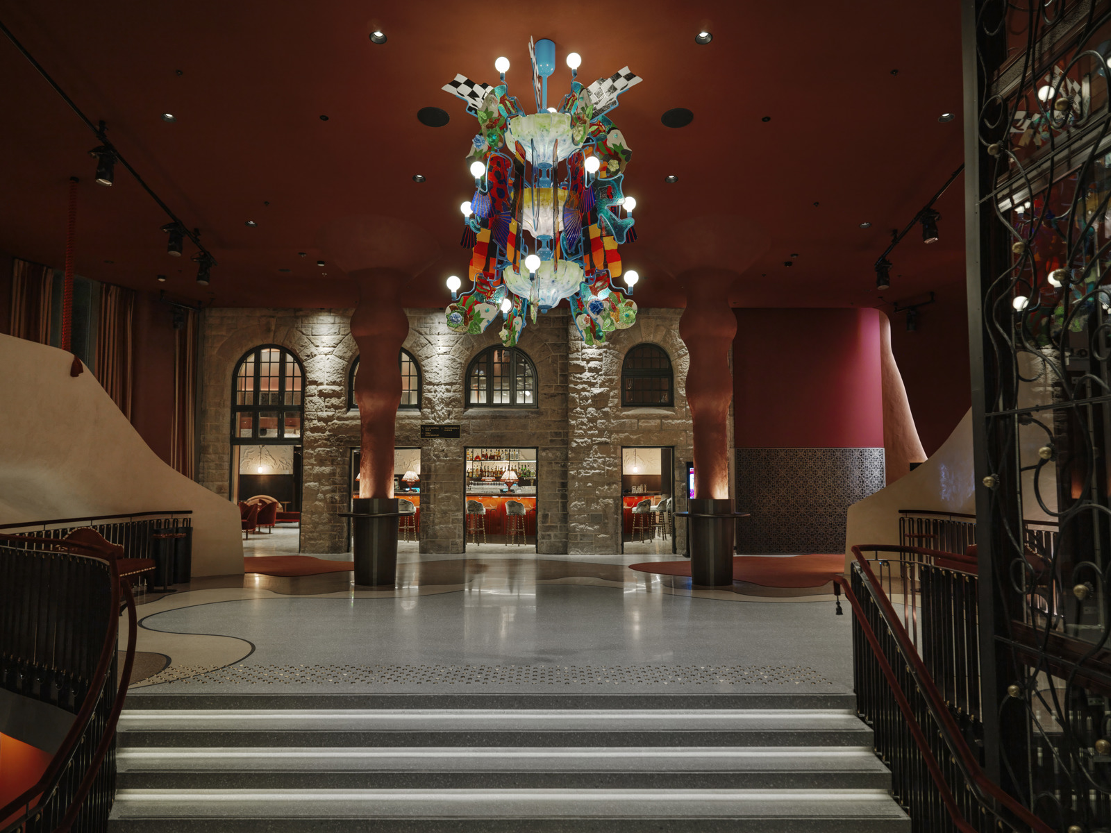Interiør foto som viser inngangshall på teater, med stor fargerik lysekrone midt i rommet, rødlige toner på interiøret.