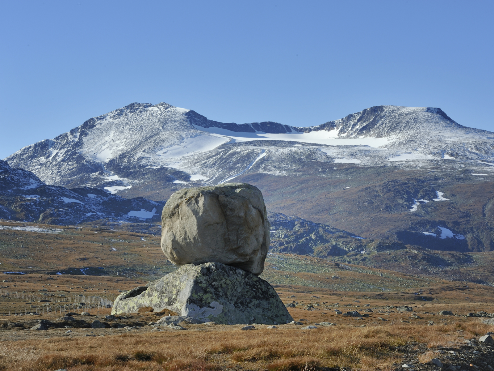 En stein på toppen av en annen stein på høyfjellet, fjell med litt snø på i bakgrunnen. Foto.