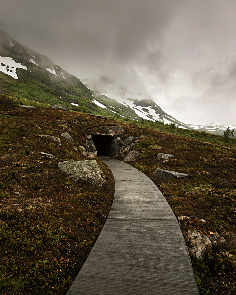 Foto av sti som leder til inngangen på et hule i fjellet.