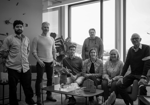 Gruppefoto av et arkitektkontor sittende og stående på kontoret sitt.