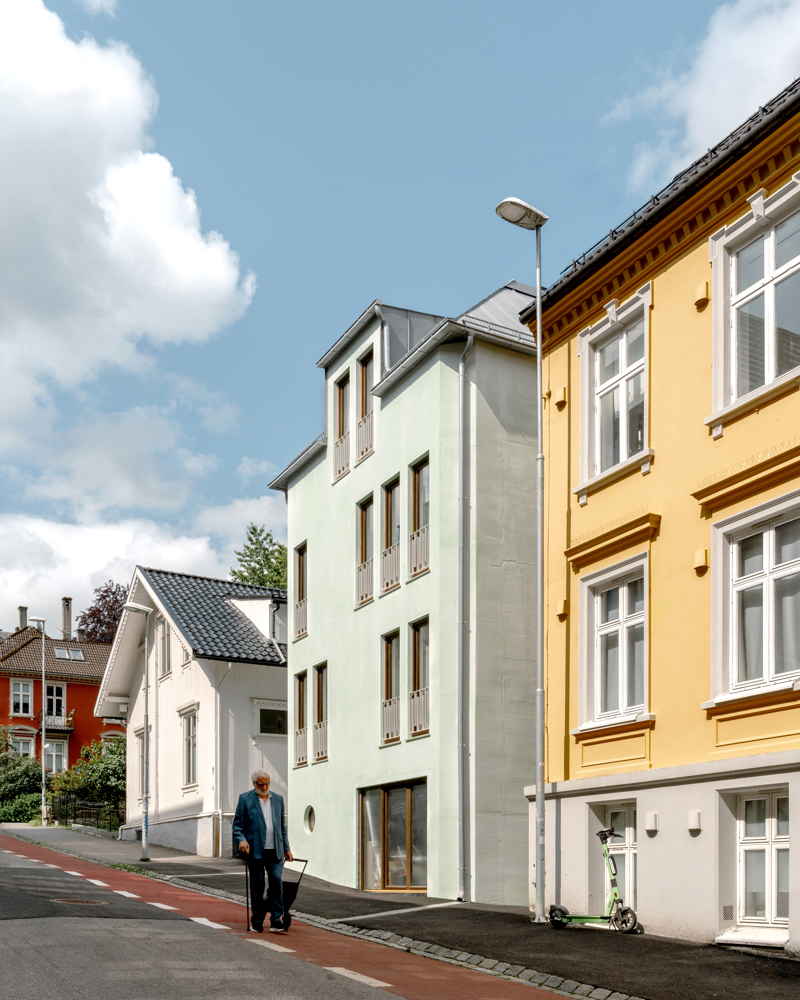 Foto av boliger langs en skrånende vei der en eldre mann går. 