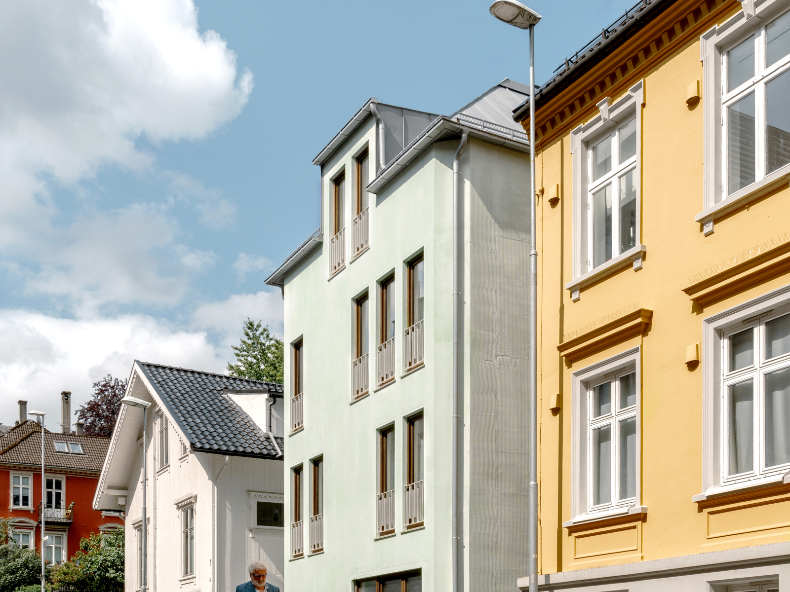 Foto av boliger langs en skrånende vei der en eldre mann går. 