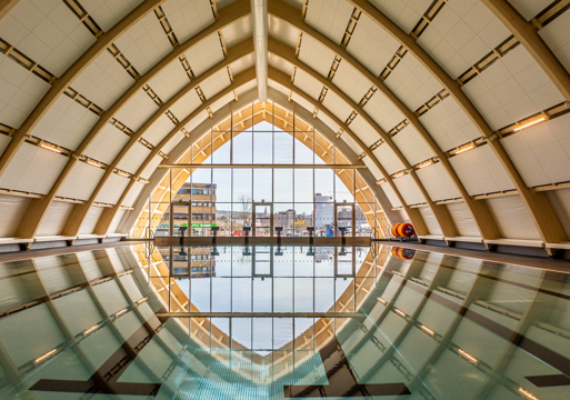 Badebasseng inne, tak formet som en trekant og store vinduer i enden av bassenget. Foto.