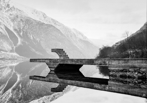 Svart hvitt fotografi av en brygge i betong med fjell ruvende i bakgrunn