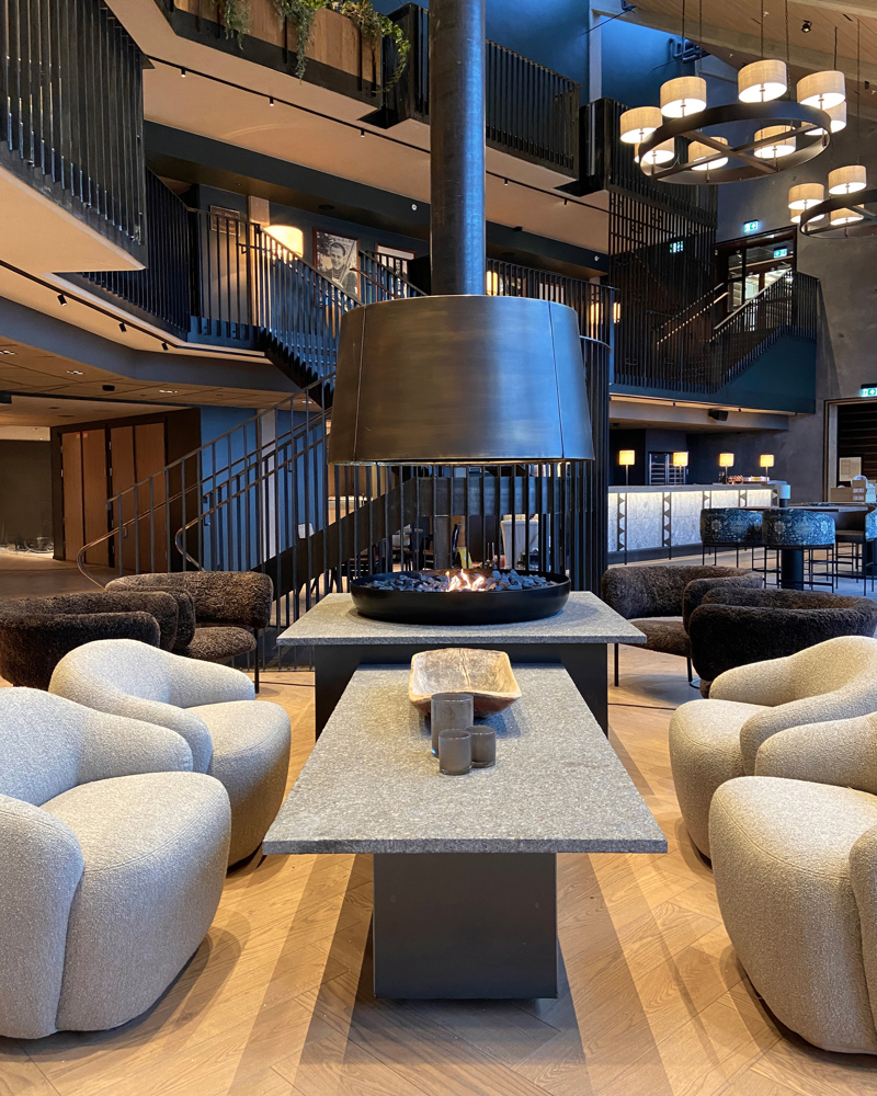 Lounge område i hotell, Åpen peis, sofastoler og trapper i bakgrunnen. Foto.