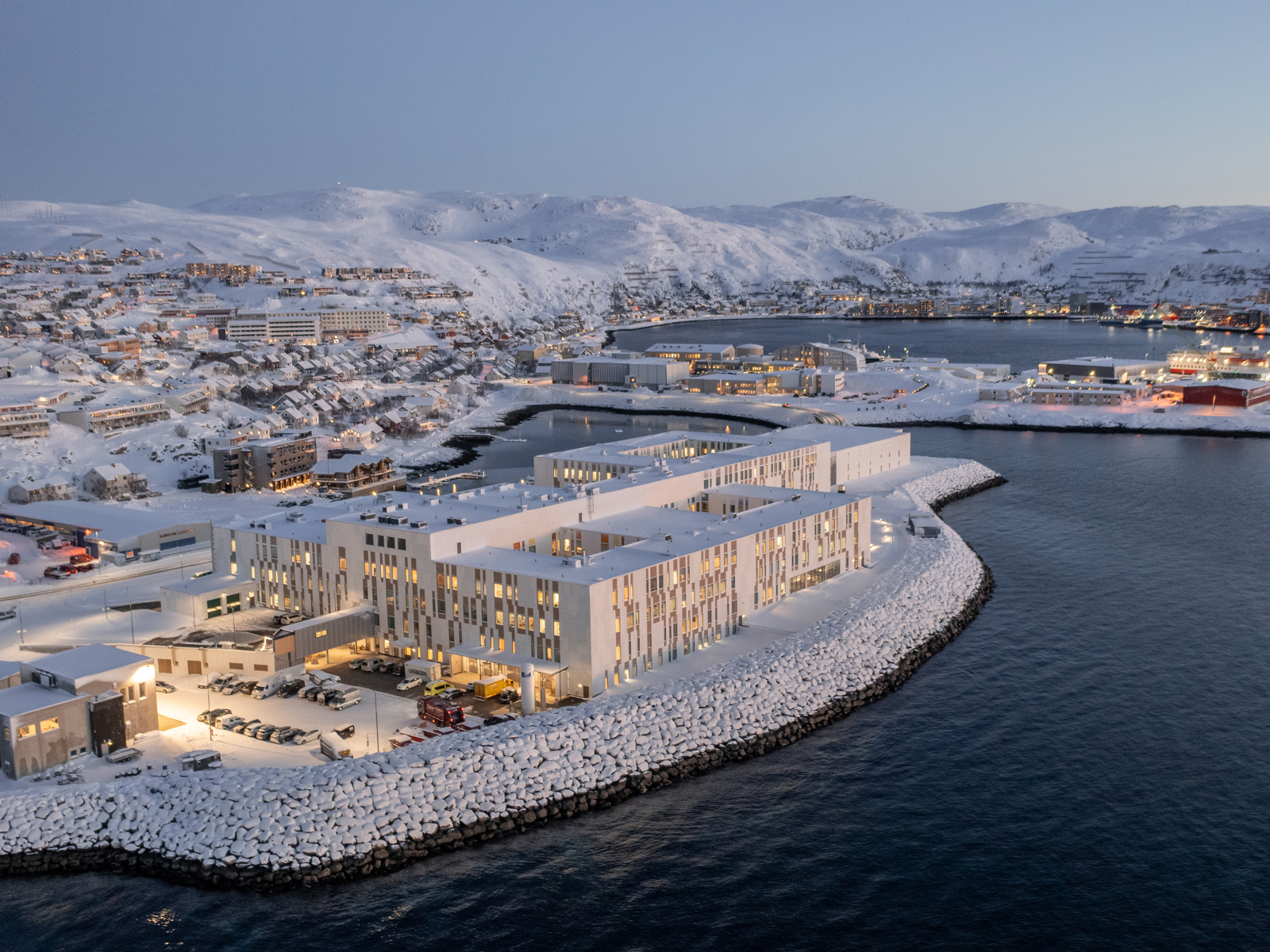 Oversiktsfoto av Hammerfest sykehus på havnekanten. Vinterlandskap med hav rundt.