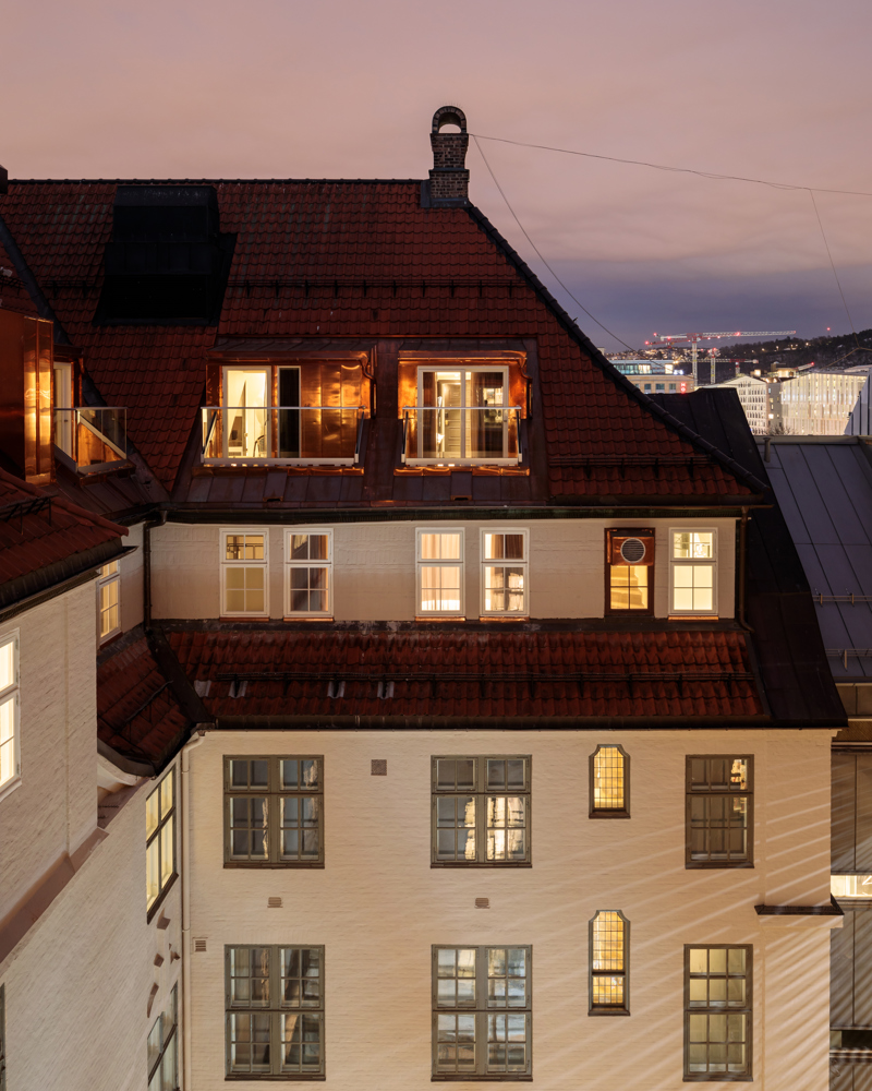 Foto av hvitt pusset tegl bygg sett fra øverste etasje på andre siden av bakgård, kveldslys.