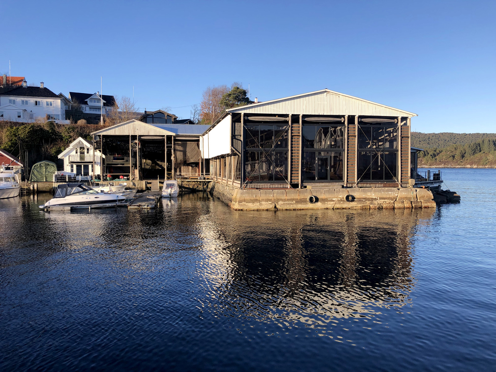 Innglasset notheng på bryggekai. Vann i forgrunnen, hus i bakgrunnen. Foto.